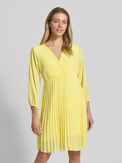 Frauenmodel trägt Knielanges Kleid mit Plisseefalten Modell 'Im44sa' von ZABAIONE in Gelb, tailliert, Wickel-Optik, Nahaufnahme Oberkörper.