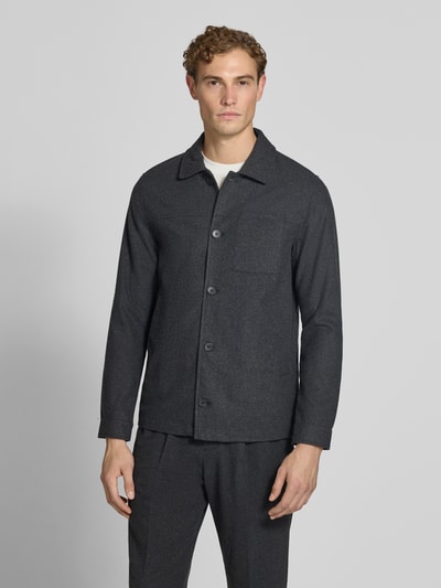 Męski model nosi Regular Fit Jacke mit Woll-Anteil od Lindbergh, ciemnoszara elastyczna mieszanka materiałów z dodatkiem wełny, wykładany kołnierz, kieszeń na piersi, listwa guzikowa, długość tyłu w rozmiarze M: 72 cm, widok całej sylwetki z przodu.
