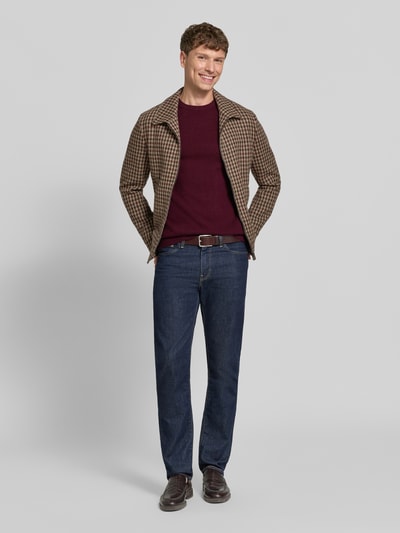 Männermodel trägt Kaschmirpullover mit gerippten Abschlüssen von Christian Berg Men in Dunkelrot, kombiniert mit brauner Jacke und Jeans, gerader Schnitt, Rundhalsausschnitt, reine Kaschmirqualität, Ganzkörperansicht von vorne.
