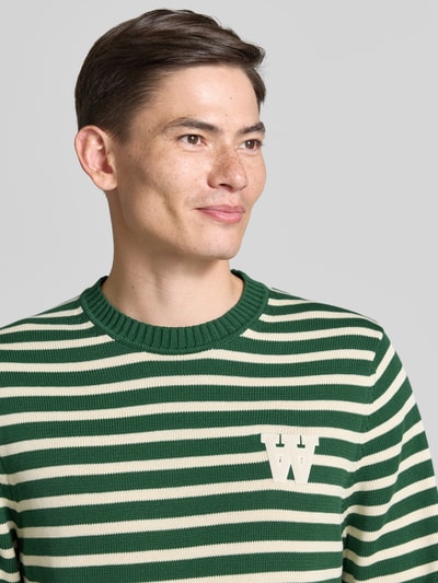Männermodel trägt Strickpullover mit Rundhalsausschnitt von Wood Wood in Grün mit cremefarbenen Streifen, Reine Baumwolle, Label-Stitching, Nahaufnahme Oberkörper.