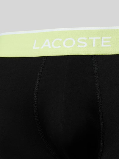 Männermodel trägt Trunks aus Baumwoll-Mix im 3er-Pack von Lacoste in Schwarz mit elastischem, gelbem Label-Bund, Nahaufnahme Oberkörper.