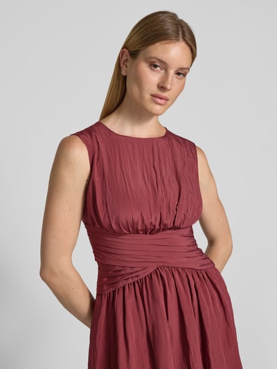 Kobiece modelka nosi sukienkę mini z mieszanki wiskozy w plisowanym wzorze od Jake*s Cocktail, taliowany krój, okrągły dekolt, krój bez rękawów, kolor bordowy, tekstura marszczona, szerokość w rozmiarze 36: 34 cm, długość tyłu w rozmiarze 36: 87 cm, zbliżenie na górną część ciała