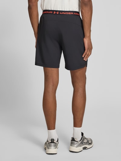 Mężczyzna model nosi szorty z logo i wpuszczanymi kieszeniami od Under Armour, krój regular fit, elastyczny pas, szerokość w rozmiarze M: 38 cm, całkowity widok z tyłu