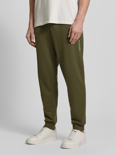 Männermodel trägt Comfort Fit Sweatpants aus katoenmix van Tommy Hilfiger in effen groen met label stitching, zijzakken, geribde boorden, ganzkörperansicht von vorne.