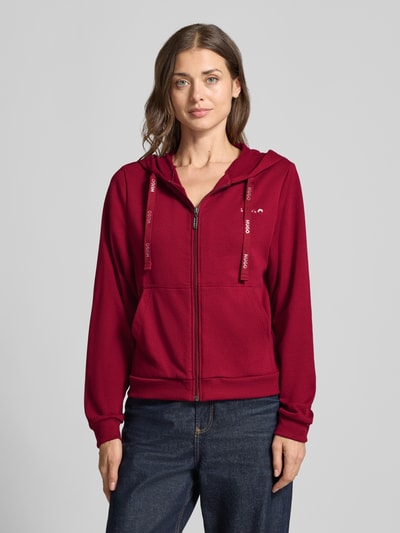 Kobieta nosi Regular Fit Sweatjacke aus Baumwoll-Mix od HUGO, kolor bordowy, prosta faktura, dżinsy, zdjęcie całej sylwetki z przodu, damska bluza.
