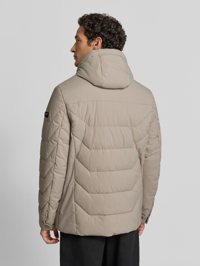 Männermodel trägt Steppjacke mit Zweiwege-Reißverschluss von bugatti in Beige, glatte Struktur, krój regular fit, Ganzkörperansicht Rückansicht. Szerokość w rozmiarze 50: 60 cm, długość pleców 75 cm, szerokość ramion 49 cm, długość rękawa 67 cm, kaptur z troczkiem, kieszenie na zamek.