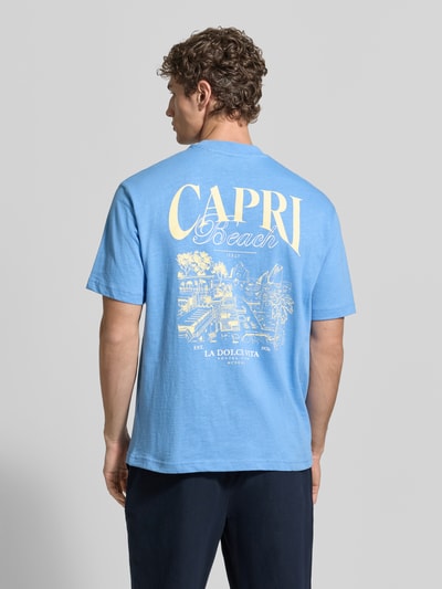 Männermodel trägt T-Shirt aus Baumwolle mit rückseitigem Print von MCNEAL in Blau mit gelbem Print, Relaxed-Fit, Ganzkörperansicht Rückansicht.