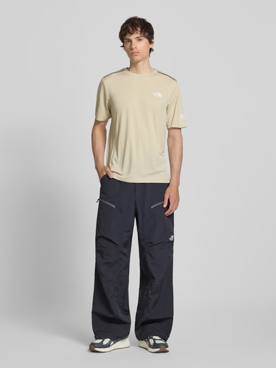 Mannenmodel draagt T-shirt met logo en ronde hals van The North Face, model 'MOUNTAIN ATHLETICS', regular fit, beige, ruglengte bij maat M 66 cm, logoprint, volledige lichaamsweergave van voren.