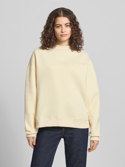 Frauenmodel trägt Relaxed Fit Sweatshirt mit Stehkragen von ANOTHER COTTON LAB aus Baumwoll-Mix in hellem Gelb, Logo-Stitching, elastische Abschlüsse, Ganzkörperansicht von vorne.