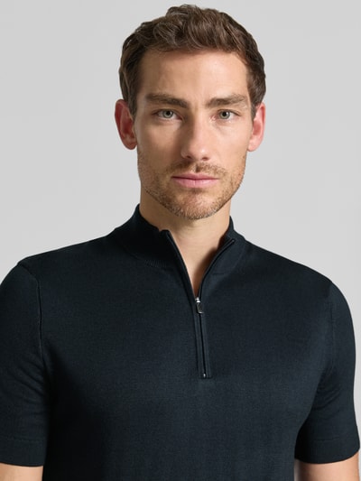 Männermodel trägt Strickshirt aus Viskose-Mix mit Stehkragen Modell 'Vadin' von JOOP!, schmaler Schnitt, Nahaufnahme Oberkörper. Körpersilhouette, Reißverschluss am Kragen, feine Textur, dunkelblau, Kontext: Herren Strickshirt, Rückenlänge 68 cm, Ärmellänge 24 cm.