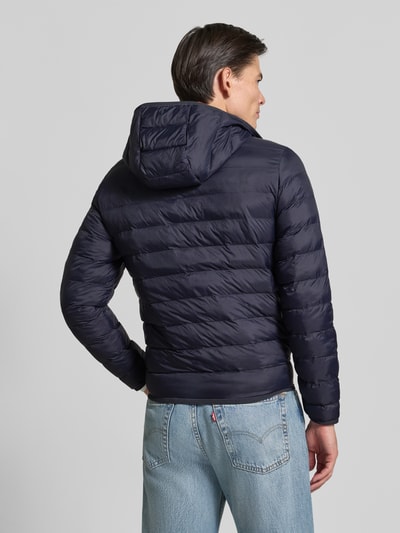 Männermodel trägt Regular Fit Bomberjacke mit down-Füllung von Lacoste in Dunkelblau, wasserabweisende Webware, Ganzkörperansicht Rückansicht.