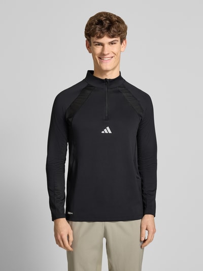 Männermodel trägt Sweatshirt mit Stehkragen von adidas Training in Schwarz, Material-Mix mit Stretch, Label-Print, Ganzkörperansicht von vorne.