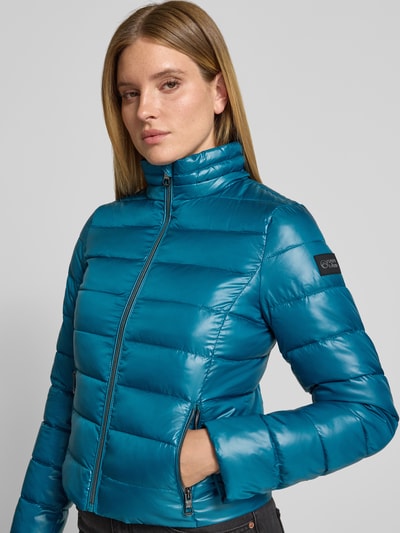 Frauenmodel trägt Regular Fit Jacke in Stepp-Optik von NAUTGÅRD in glänzendem Petrolblau mit Reißverschluss, Nahaufnahme Oberkörper. Rückenlänge 55 cm, Schulterbreite 39 cm, Brustweite 49 cm, Ärmellänge 63 cm.