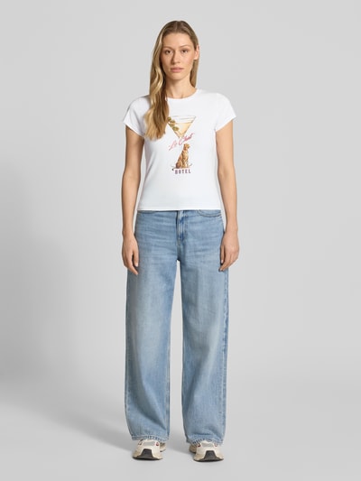 Frauenmodel trägt T-Shirt mit Label-Detail Modell 'LEOPARDTINI' von Guess in Weiß, körpernaher Schnitt, Baumwoll-Elasthan-Mix, Rundhalsausschnitt, Ganzkörperansicht von vorne.