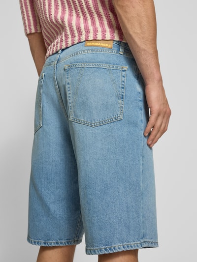 Männermodel trägt Loose Fit Jeansshorts aus Lyocell-Baumwoll-Mix Modell 'BAGGY HEMP BLEND' von Armedangels, hellblauer Denim mit Label Patch, sichtbare Gürtelschlaufen und 5-Pocket-Design, Ganzkörperansicht Rückansicht.