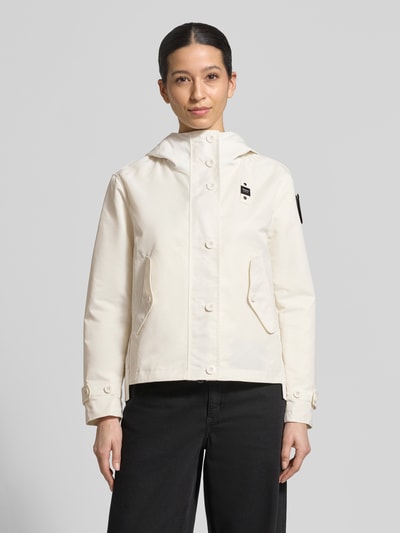 Frauenmodel trägt helle Jacke mit Label-Patches Modell 'MARCELA' von Blauer Usa, gerader Schnitt, Kapuze, Knopfverschluss, Ganzkörperansicht von vorne.