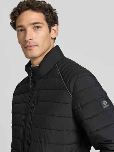Männermodel trägt Steppjacke mit Stehkragen und Reißverschlusstaschen von LERROS, schwarze Farbe, glatte Struktur, Nahaufnahme Oberkörper. Regular Fit, sichtbare Reißverschlusstaschen und Logo, Kontext: Rückenlänge 69 cm, Schulterbreite 46 cm, Brustweite 60 cm, Ärmellänge 69 cm.