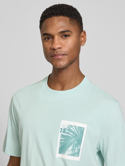 Männermodel trägt Regular Fit T-Shirt aus reiner Baumwolle Modell 'TE_BOARD' von BOSS Orange in Mintgrün mit Foto-Print, Nahaufnahme Oberkörper.