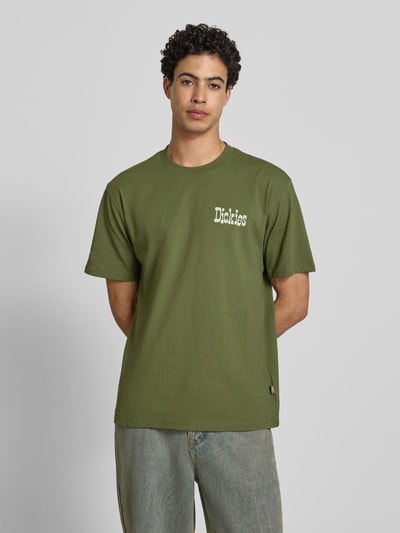 Männermodel trägt Herren T-Shirt mit Logo Modell 'VERNAL' von Dickies in Grün, Reine Baumwolle, Relaxed-Fit, Rundhalsausschnitt, Ganzkörperansicht von vorne.