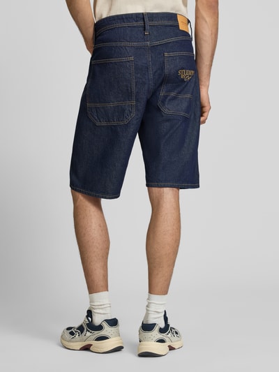 Männermodel trägt Jeansshorts im 5-Pocket-Design Modell 'ALEX' von Jack & Jones aus reiner Baumwolle, Straight Fit, Dunkelblau, Ganzkörperansicht Rückansicht, Bundweite bei Größe M 44 cm, Innenbeinlänge 30 cm.