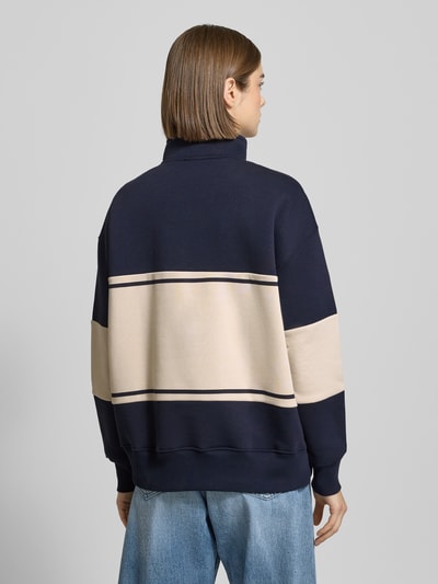 Frauenmodel trägt Sweatshirt mit Reißverschluss Modell 'Cosette' von LeGer by Lena Gercke im Baumwoll-Mix mit navy-beigen Streifen, Relaxed Fit, Stehkragen und Stitching, Ganzkörperansicht Rückansicht.