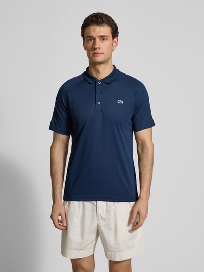 Męski model nosi Regular Fit Sport Poloshirt mit Label Patch von Lacoste, efekt: jednolity kolor, krój regular fit, naszywka z logo, kołnierzyk polo, zapięcie na 3 guziki, krótki rękaw, wykończenie materiału: pika, Ganzkörperansicht von vorne.