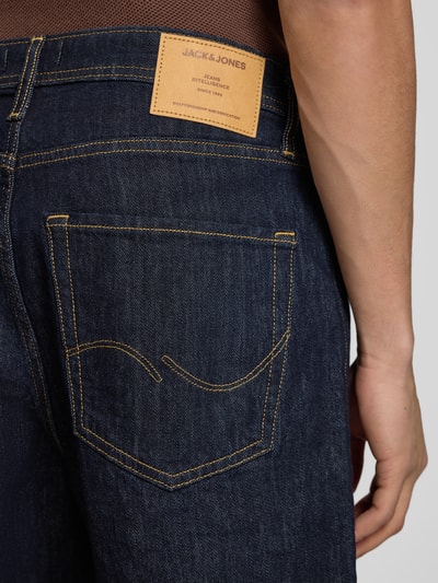 Männermodel trägt Relaxed Fit Jeansshorts Modell 'TONY' von Jack & Jones aus Baumwoll-Elasthan-Mix, dunkles Blau, Detailaufnahme Rückansicht, Eingrifftaschen, Bundweite bei Größe M 42 cm, Innenbeinlänge 21 cm.
