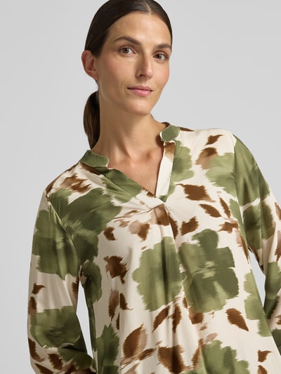 Frauenmodel trägt Relaxed Fit Bluse aus reiner Viskose Modell 'Lari' von ZABAIONE mit grün-braunem Muster, Nahaufnahme Oberkörper. Reine Viskose, Serafino-Ausschnitt, langärmelig, Rückenlänge bei Größe S 55 cm, Ärmellänge 57 cm.