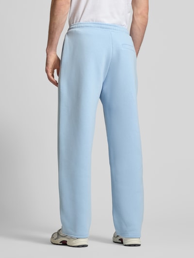 Męski model nosi spodnie dresowe Sweatpants aus Baumwoll-Mix von REVIEW w jasnoniebieskim kolorze, prosty krój, elastyczny pas, boczne i tylne kieszenie, detal z logo, długość wewnętrzna nogawki w rozmiarze M: 77 cm, całkowity widok z tyłu.