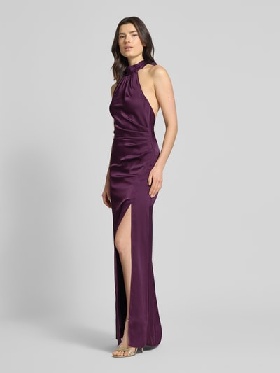 Frauenmodel trägt Regular Fit Abendkleid mit Raffungen von Jake*s Cocktail aus violettem Satin, Halterneck, Rückenausschnitt, Gehschlitz, ärmelloses Design, Rückenlänge 175 cm, Brustweite 35 cm, Ganzkörperansicht von vorne.