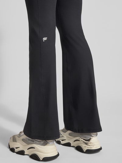 Frauenmodel trägt schwarze Flared Fit Leggins mit Logo-Print Modell 'OASIS' von Fabletics, elastischer Bund, Rückansicht, Detailaufnahme.