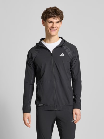 Männermodel trägt schwarze Sweatjacke mit Stretch-Anteil Modell 'TECH' von adidas, gerader Schnitt, Kapuze, Ganzkörperansicht von vorne, Climacool-Technologie, elastischer Material-Mix.