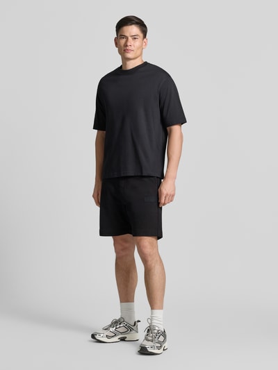 Männermodel trägt schwarze Regular Fit Sweatshorts aus Baumwoll-Mix Modell 'JT_SHORTS' von BOSS Green, schlichte Struktur, Ganzkörperansicht von vorne