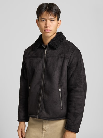 Männermodel trägt Jacke in Leder-Optik mit Reißverschlusstaschen von REVIEW, schwarze Farbe, Umlegekragen, Ganzkörperansicht von vorne.