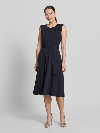 Modelka kobieca ma na sobie 'Cocktailkleid mit Bindegürtel' od Christian Berg Woman Selection, granat, okrągły dekolt, drapowania, pasek, krój slim fit, długość midi, elastyczny materiał, długość pleców w rozmiarze 36: 105 cm, szerokość w rozmiarze 36: 33 cm, widok całej sylwetki z przodu