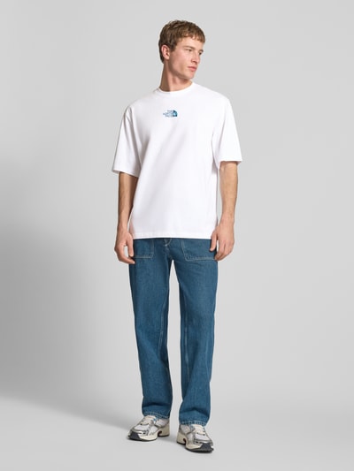 Męski model nosi Oversized T-Shirt mit Logo und Rundhalsausschnitt von The North Face, czysta bawełna, oversize, logo, okrągły dekolt, długość tyłu w rozmiarze M: 73 cm, całopostaćowy widok z przodu.