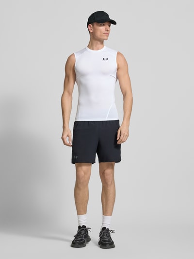 Męski model nosi Slim Fit Top mit Logo-Print von Under Armour, elastyczna mieszanka materiałów, okrągły dekolt, długość tyłu 65 cm w rozmiarze M, krój slim fit, nadruk z logo, całopostaciowy widok z przodu.