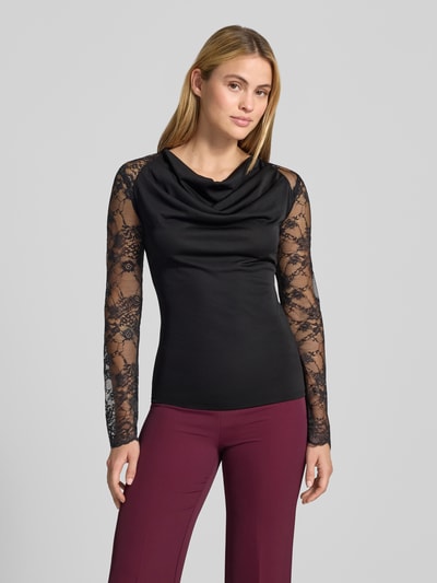 Kobiece modelka nosi Slim Fit Longsleeve mit Spitzenbesatz von Rinascimento, czarny, półprzezroczysty materiał, lejący kołnierz, obszycie koronką, długość tyłu w rozmiarze S: 60 cm, widok z przodu całej sylwetki.