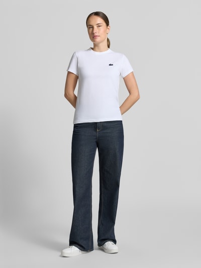 Vrouwenmodel draagt wit Slim Fit Sport-T-Shirt aus Baumwoll-Mix van Lacoste, donkere jeans, dames sport-t-shirt, volledig frontaal.