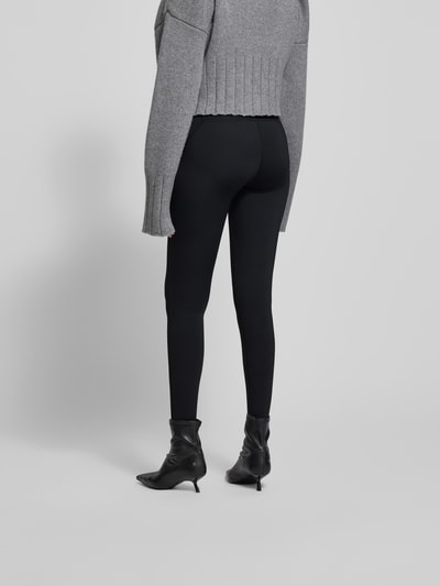 Frauenmodel trägt Leggings mit elastischem Logo-Bund von black palms, schwarzer Material-Mix mit Stretch-Anteil, körpernaher Schnitt, Ganzkörperansicht Rückansicht.