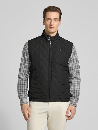 Männermodel trägt Regular Fit Weste mit Stehkragen in Stepp-Optik von Gant, schwarz, Logo-Stitching, Reißverschluss, Ganzkörperansicht von vorne.