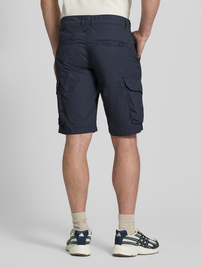 Mężczyzna nosi Bermudas mit Cargotaschen von camel active, bawełna, krój regular fit, szerokość w rozmiarze 32: 44 cm, długość nogawki 26 cm, kolor granatowy, tekstura gładka, widoczne kieszenie cargo, detal z logo, widok całej sylwetki z tyłu.