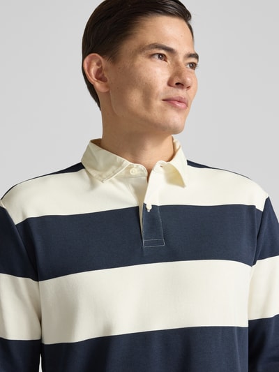 Męski model nosi Koszulkę polo z krótką listwą guzikową od MCNEAL z mieszanki bawełny, krój regular fit, kołnierzyk polo, prążkowane zakończenia rękawów, długość tyłu 71 cm, rozmiar M, szerokie paski granatowo-kremowe, tekstura gładka, ujęcie: zbliżenie na górną część ciała.