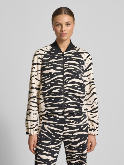 Kobiece modelka nosi Jacke im Allover-Look mit Zweiwege-Reißverschluss od Marc Cain w kolorach czarnym i kremowym, materiał elastyczny, regular fit, wzór zwierzęcy, widok całej sylwetki z przodu.