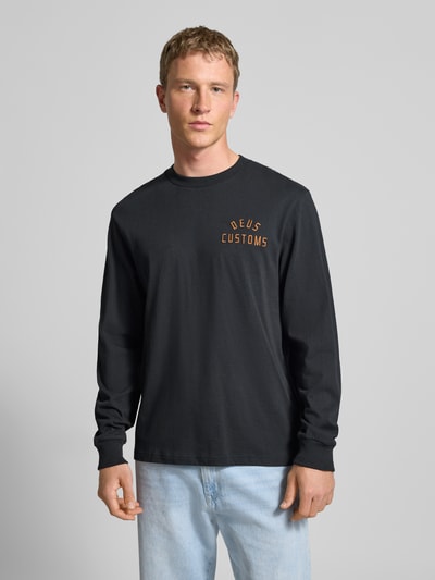 Männermodel draagt Regular Fit Shirt met lange mouwen met logostitching Model 'Engineer' van DEUS EX MACHINA, puur katoen, ronde hals, elastische mouwboorden, ruglengte maat M 70 cm, zwart met oranje detail, vooraanzicht bovenlichaam.