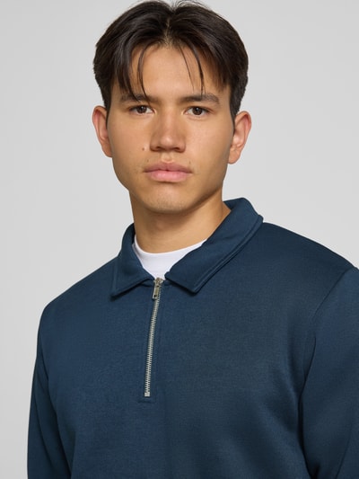 Mężczyzna nosi Regular Fit Sweatshirt mit Baumwoll-Anteil Modell 'Bradley' von JACK & JONES, Mieszanka materiałów, kołnierz zapinany, zamek błyskawiczny, głęboki niebieski kolor, gładka tekstura, kontekst: Długość tyłu w rozmiarze M: 69 cm, zdjęcie: zbliżenie na górną część ciała.