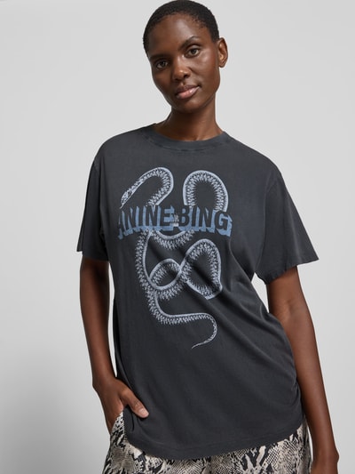 Frauenmodel trägt Slim Fit T-Shirt aus reiner Baumwolle von Anine Bing in Dunkelgrau mit Label-Print, Rundhalsausschnitt, kurzärmelig, Rückenlänge 66 cm, Ganzkörperansicht von vorne.
