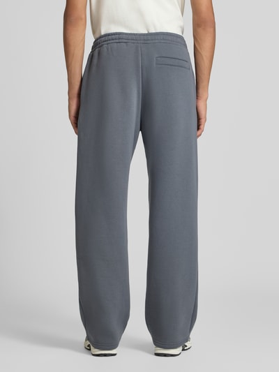 Männermodel trägt Sweatpants mit Logo-Print und Gesäßtasche von REVIEW in Grau, Baumwoll-Mix, gerader Schnitt, Ganzkörperansicht Rückansicht.