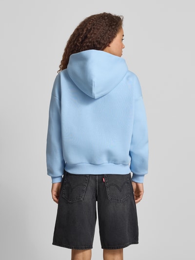 Kobiece model nosi Relaxed Fit Sweatjacke mit Kapuze od REVIEW, niebieska bawełna, kaptur, kieszenie kangurki, nadruk logo, luźny krój, widok całej sylwetki z tyłu.