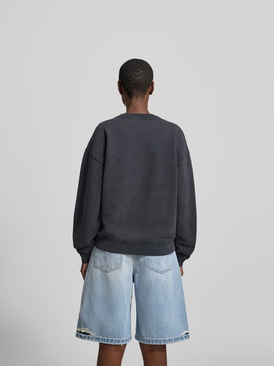 Frauenmodel trägt Regular Fit Sweatshirt mit Motiv-Print von Anine Bing, reine Baumwolle, Rundhalsausschnitt, elastische Abschlüsse, Rückenlänge 59 cm, Farbe Dunkel, strukturierte Oberfläche, Ganzkörperansicht Rückansicht.